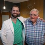 Dr. Austin L. Lyman with arm around older male patient in plaid shirt at reception area