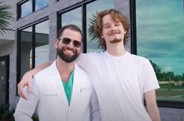 Dr. Austin L. Lyman posing with young male patient outside modern dental office building