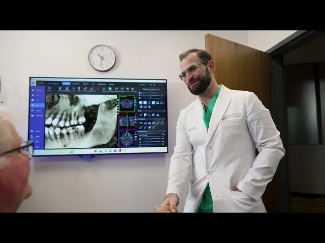 Dr. Austin L. Lyman reviewing panoramic dental X-ray and 3D scan with patient on large monitor
