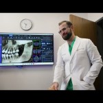 Dr. Austin L. Lyman reviewing panoramic dental X-ray and 3D scan with patient on large monitor