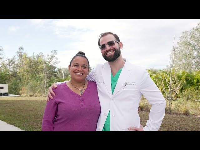 Dr. Austin Lyman in white coat posing with smiling female patient outdoors