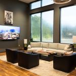 Modern waiting lounge with sectional sofa, dark chairs, TV, large windows, and hardwood floors